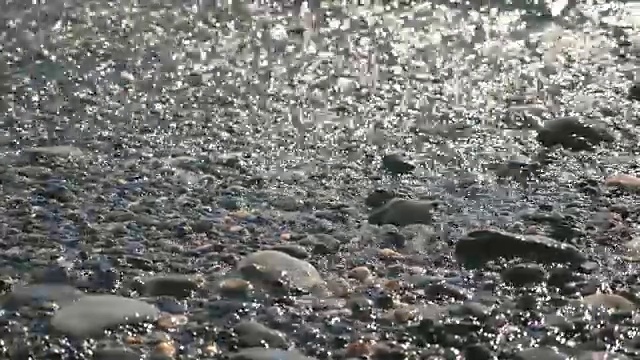 在阳光明媚的日子里，温和的海浪拍打着卵石滩。美丽的海景背景。假期的概念。近距离视频素材