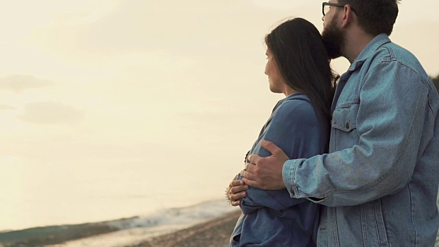 相爱的男人和女人拥在一起，看着夕阳下的海浪视频素材