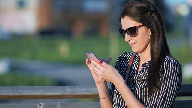 迷人的女人坐在城市公园的长椅上使用智能手机视频素材