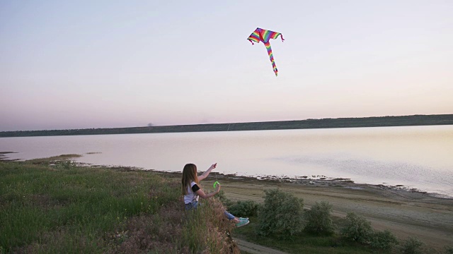 快乐的年轻女子在一个湖泊背景的林间空地上玩风筝在夏季日落视频素材