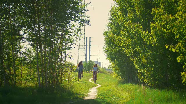 年轻的女孩们骑着自行车到森林里散步视频素材