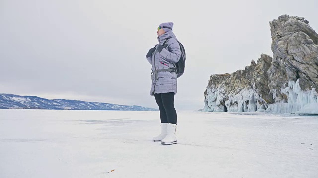 女人在贝加尔湖冰面上的旅行。冬岛之旅。女孩在冰岩石下行走。游客看着美丽的冰洞。极限跋涉和步行。背包客在大自然中休憩。视频素材