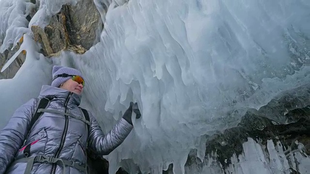 女人在贝加尔湖冰面上的旅行。冬岛之旅。女孩在冰岩石下行走。游客看着美丽的冰洞。极限跋涉和步行。背包客在大自然中休憩。视频素材