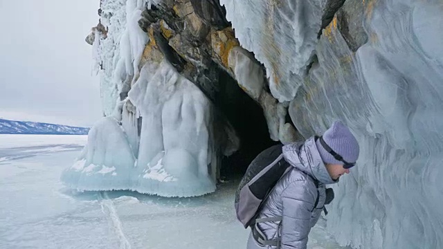 女人在贝加尔湖冰面上的旅行。冬岛之旅。女孩在冰岩石下行走。游客看着美丽的冰洞。极限跋涉和步行。背包客在大自然中休憩。视频素材