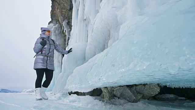 女人在贝加尔湖冰面上的旅行。冬岛之旅。女孩在冰岩石下行走。游客看着美丽的冰洞。极限跋涉和步行。背包客在大自然中休憩。视频素材