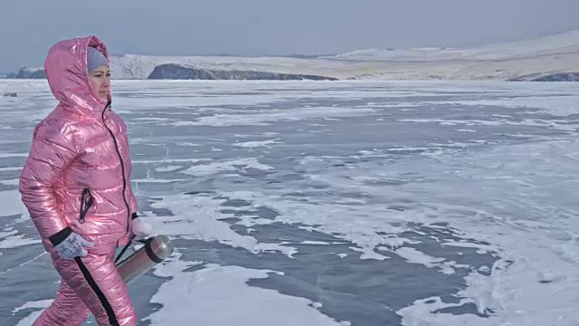 一个女孩走在贝加尔湖破裂的冰面上。一名女旅行者探索并看着一块浮冰。这是自然界中最神奇最纯净的地方。冰环绕着旅行者所有的旅程。视频素材