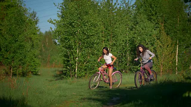 在一个阳光明媚的日子里，美丽的女孩骑着自行车在绿树的背景上视频素材