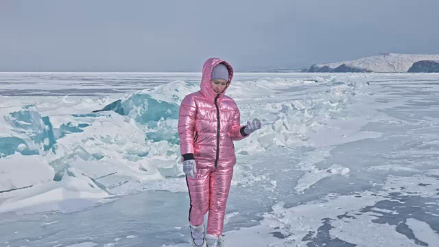 一个女孩走在贝加尔湖破裂的冰面上。一名女旅行者探索并看着一块浮冰。这是自然界中最神奇最纯净的地方。冰环绕着旅行者所有的旅程。视频素材