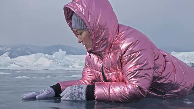 一个女孩走在贝加尔湖破裂的冰面上。一名女旅行者探索并看着一块浮冰。这是自然界中最神奇最纯净的地方。冰环绕着旅行者所有的旅程。视频素材