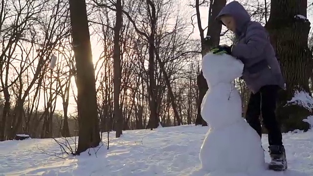 男孩在冬季公园堆雪人的慢镜头视频素材