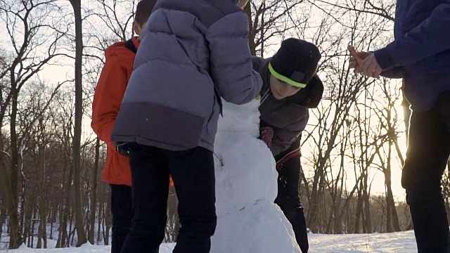 四个男孩在冬季公园做雪人的慢镜头视频素材