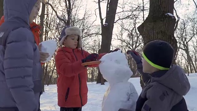 男孩们在冬天的公园堆雪人，慢镜头视频素材