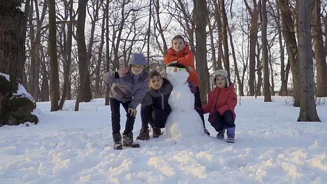 四个高加索男孩在冬季公园和雪人摆姿势照相视频素材