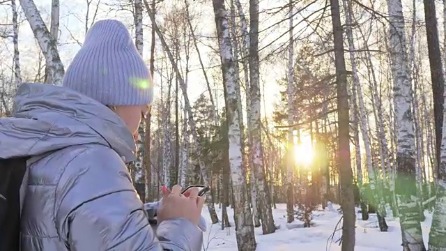 一个女人走在树林里。旅行者在森林里用手机拍照。女孩会自拍，用智能手机交流。美丽多汁的日落时分。视频素材