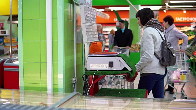 一位年轻女子在商店里用电子秤称蔬菜。视频素材