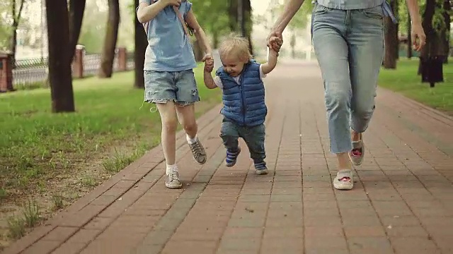 妈妈带着年幼的儿子和女儿在公园里跑步。视频素材