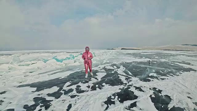 一个女孩走在贝加尔湖破裂的冰面上。一名女旅行者探索并看着一块浮冰。这是自然界中最神奇最纯净的地方。冰环绕着旅行者所有的旅程。视频素材