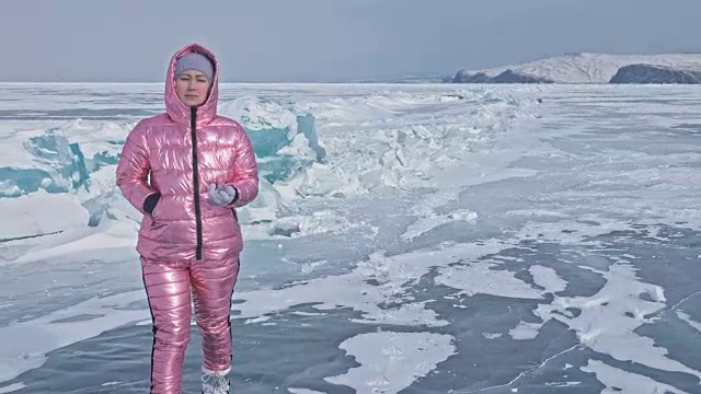 一个女孩走在贝加尔湖破裂的冰面上。一名女旅行者探索并看着一块浮冰。这是自然界中最神奇最纯净的地方。冰环绕着旅行者所有的旅程。视频素材