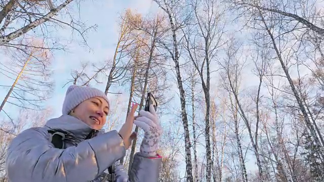 一个女人走在树林里。旅行者在森林里用手机拍照。女孩会自拍，用智能手机交流。美丽多汁的日落时分。视频素材