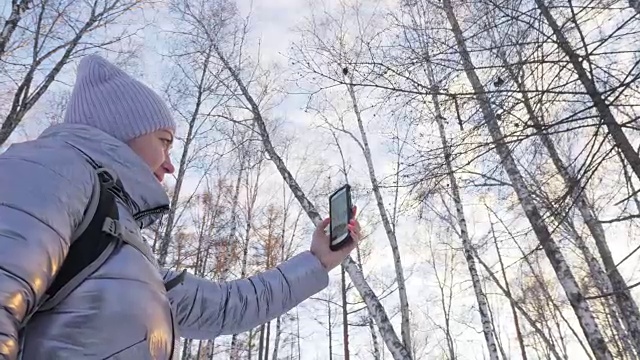 一个女人走在树林里。旅行者在森林里用手机拍照。女孩会自拍，用智能手机交流。美丽多汁的日落时分。视频素材