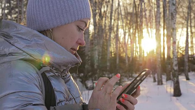 一个女人走在树林里。旅行者在森林里用手机拍照。女孩会自拍，用智能手机交流。美丽多汁的日落时分。视频素材