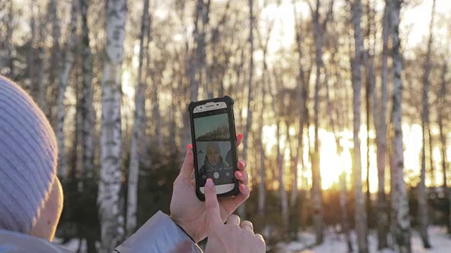 一个女人走在树林里。旅行者在森林里用手机拍照。女孩会自拍，用智能手机交流。美丽多汁的日落时分。视频素材