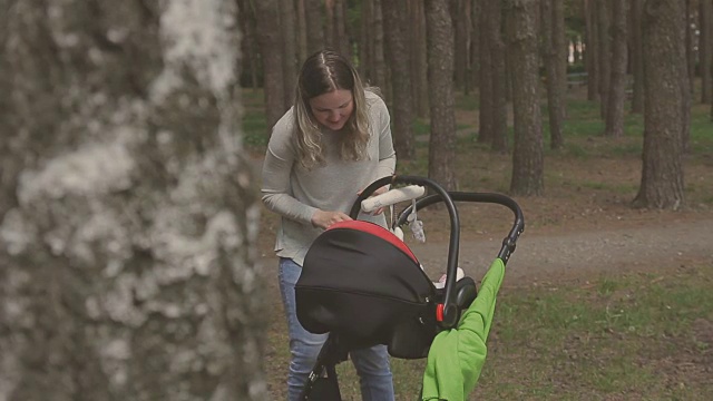 美丽的女人在公园里推着婴儿车和她的小女儿散步视频素材