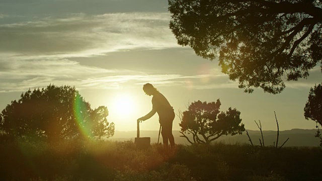 日落时分，一个女人的剪影摆好了木头，然后用斧头砍了它视频素材