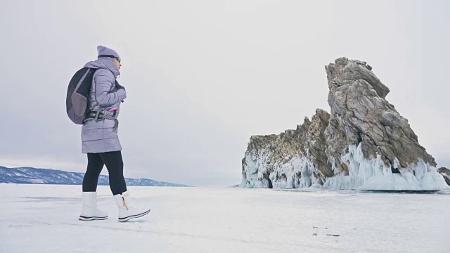 女人在贝加尔湖冰面上的旅行。冬岛之旅。女孩在冰岩石下行走。游客看着美丽的冰洞。极限跋涉和步行。背包客在大自然中休憩。视频素材