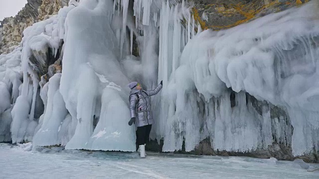 女人在贝加尔湖冰面上的旅行。冬岛之旅。女孩在冰岩石下行走。游客看着美丽的冰洞。极限跋涉和步行。背包客在大自然中休憩。视频素材