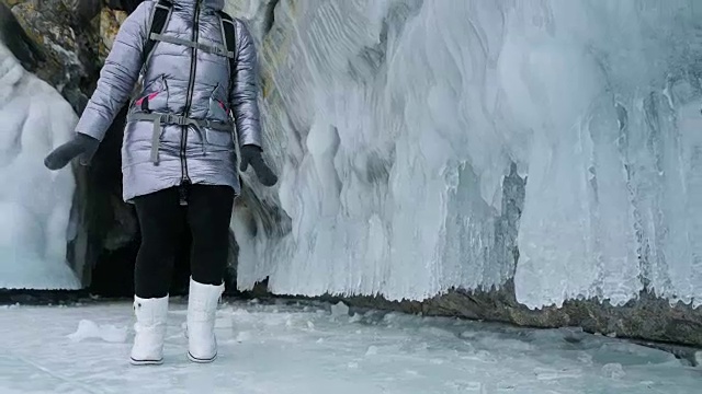 女人在贝加尔湖冰面上的旅行。冬岛之旅。女孩在冰岩石下行走。游客看着美丽的冰洞。极限跋涉和步行。背包客在大自然中休憩。视频素材