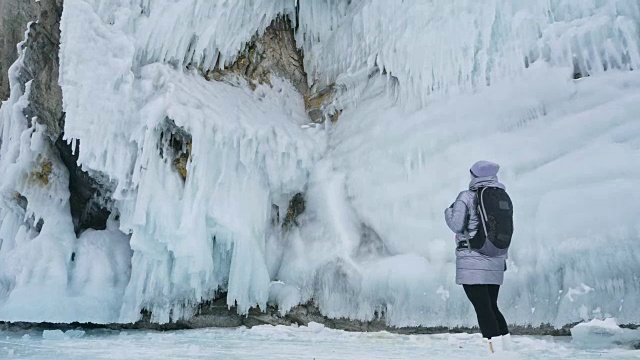 女人在贝加尔湖冰面上的旅行。冬岛之旅。女孩在冰岩石下行走。游客看着美丽的冰洞。极限跋涉和步行。背包客在大自然中休憩。视频素材