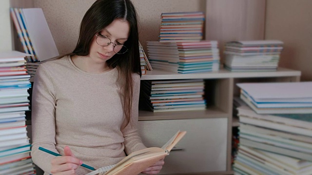 一个戴眼镜的黑发女人坐在地板上的书中写着纸条。视频素材