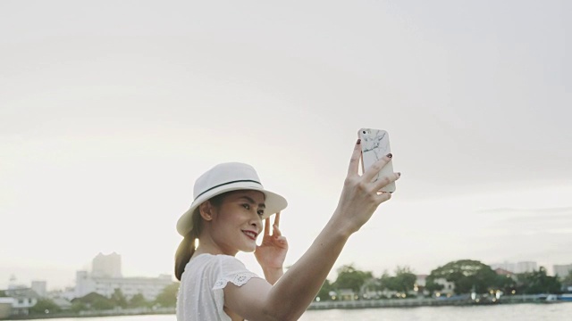 傍晚阳光明媚的泰国妇女在河边用智能手机自拍视频素材