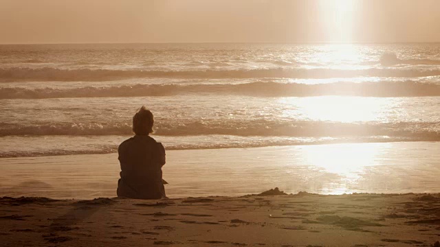 老女人在海滩上看太阳在海洋上落下的后视图视频素材