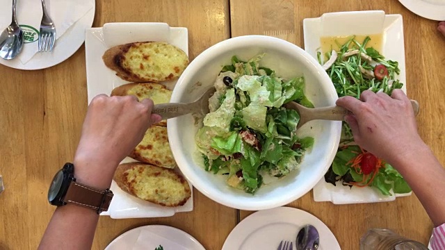 女人的手混合美味的超级食物凯撒沙拉配料与木汤匙在桌子上的餐厅大蒜面包和食物集。烹饪概念。前视图。视频素材