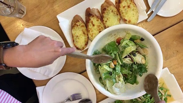 女人的手混合美味的超级食物凯撒沙拉配料与木汤匙在桌子上的餐厅大蒜面包和食物集。烹饪概念。前视图。视频素材