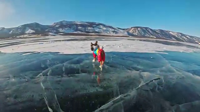 玩具小猎犬穿着滑稽的衣服和鞋子在裂缝里美丽的冰上玩球。妈妈和女儿穿着运动服和花样滑冰鞋。女孩们把玩具扔给狗。狗玩游戏。视频素材