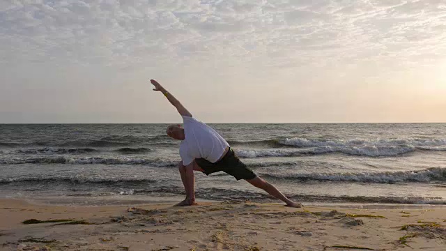 男子站立瑜伽姿势乌提塔parsvakonasana在海滩上的背景波视频素材