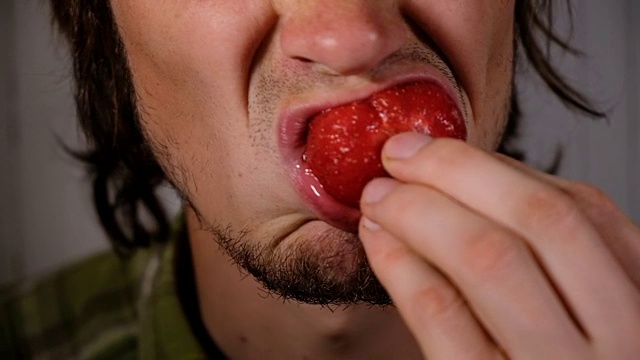 残忍的男人正在吃多汁的草莓特写。一个恶心的饥肠辘辘的家伙恶心地嚼着一颗成熟的大浆果视频素材