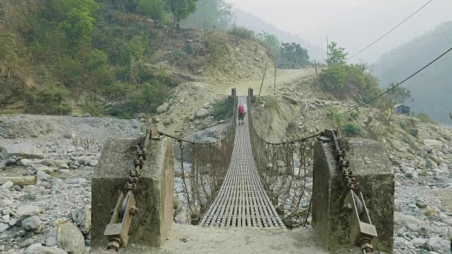 两名背包客在尼泊尔的一座悬空金属桥上行走。视频素材