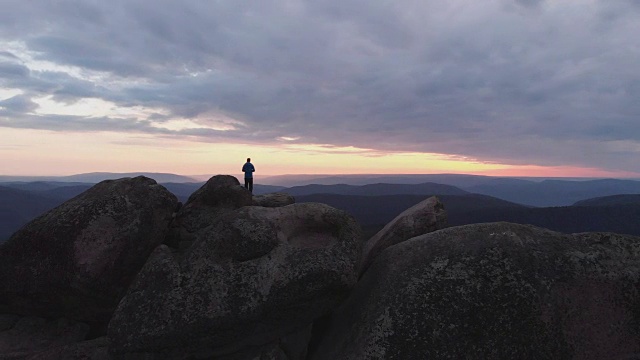 一个孤独的人站在悬崖顶上欣赏夕阳的鸟瞰图。视频素材