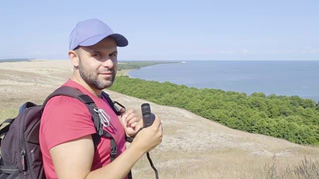 用双筒望远镜观察野生动物的旅行者。男人们在度假中观赏自然景观。一个背包旅行者正在用双筒望远镜看大海，看美丽的风景。山。海滩。视频素材