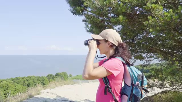 用双筒望远镜观察野生动物的旅行者。女人在度假看自然景观。一个背包旅行者正在用双筒望远镜看大海，看美丽的风景。山。海滩。视频素材