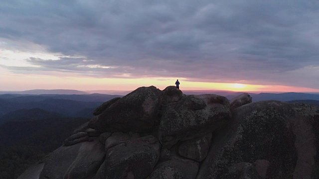 一个孤独的人站在悬崖顶上欣赏夕阳的鸟瞰图。视频素材