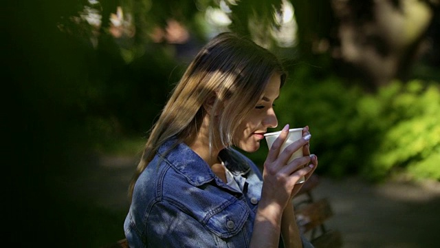 年轻美丽的女人喝咖啡放松在夏季公园的长凳上视频素材