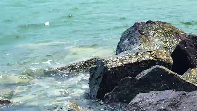 海浪和岸上的大石头。蓝色和透明的水在海洋岩石海滩的背景。海浪在岩石岛岸边视频素材