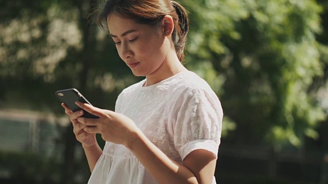 东南亚美女正在用智能手机上网，在花园里和朋友聊天视频素材