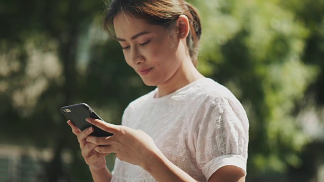 泰国美女正在花园里用智能手机上网和和朋友聊天视频素材