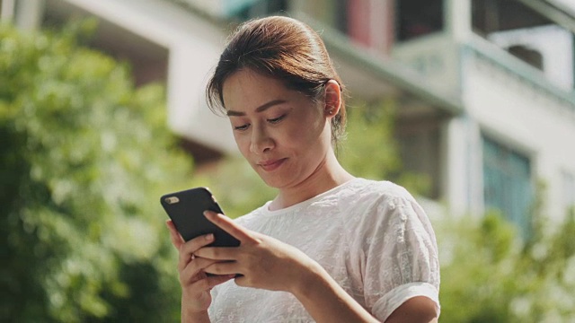 亚洲美女正在使用智能手机上网和聊天的朋友在花园里视频素材